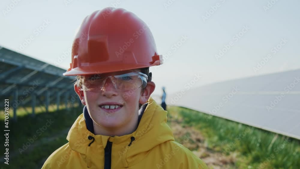 Young cute boy wearing helmet walking between solar panels. Little kid visiting modern huge power station with family on rural field. Young cute boy wearing helmet walking between solar panels. Little kid visiting modern huge power station with family on rural field.