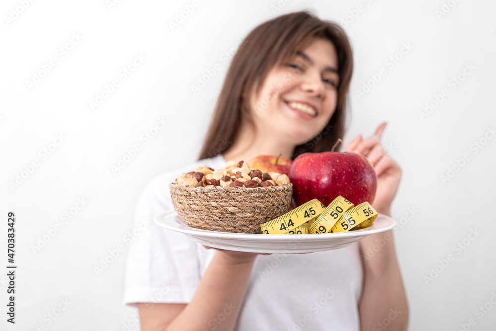 A plate with apples, nuts and a measuring tape in the hands of a young woman.