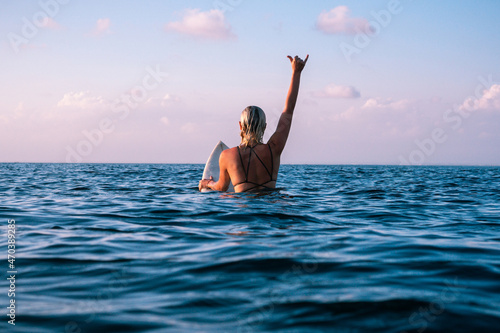 Portrait of surfer girl with beautiful body on surfboard in the ocean at colourful sunset time