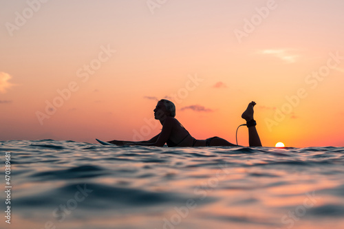 Portrait of surfer girl with beautiful body on surfboard in the ocean at colourful sunset time © Lila Koan