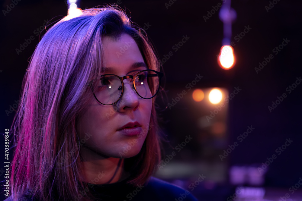 Cute young woman in a dark room with colored lights wearing glasses. Cute young woman in a dark room with colored lights wearing glasses.