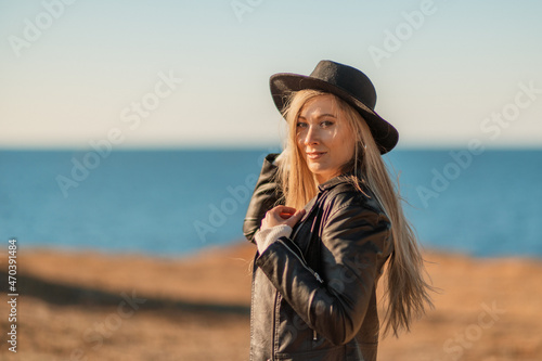 A blonde in a stylish black leather jacket walks along the seashore.