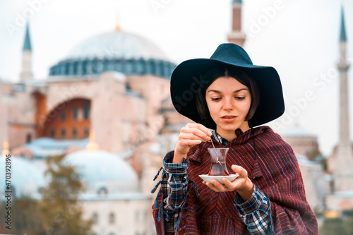 A young girl in a burgundy poncho and a hat holds traditional Turkish tea