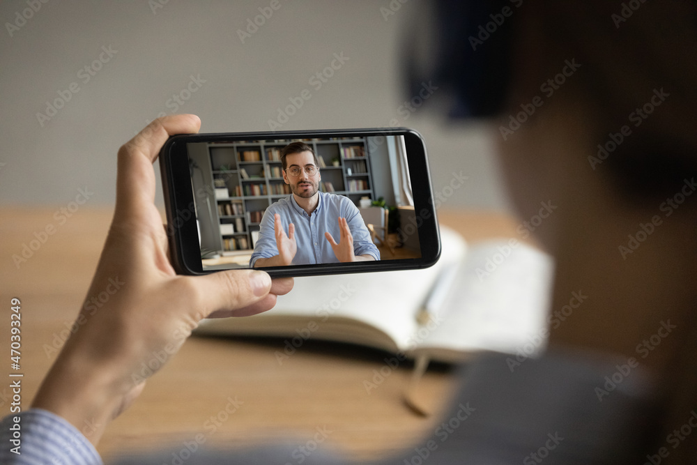 Two colleagues talk through videocall, close up smartphone screen over female shoulder. Woman listen webinar, gain new knowledge watch video, male coach tell share experience. Video call event concept