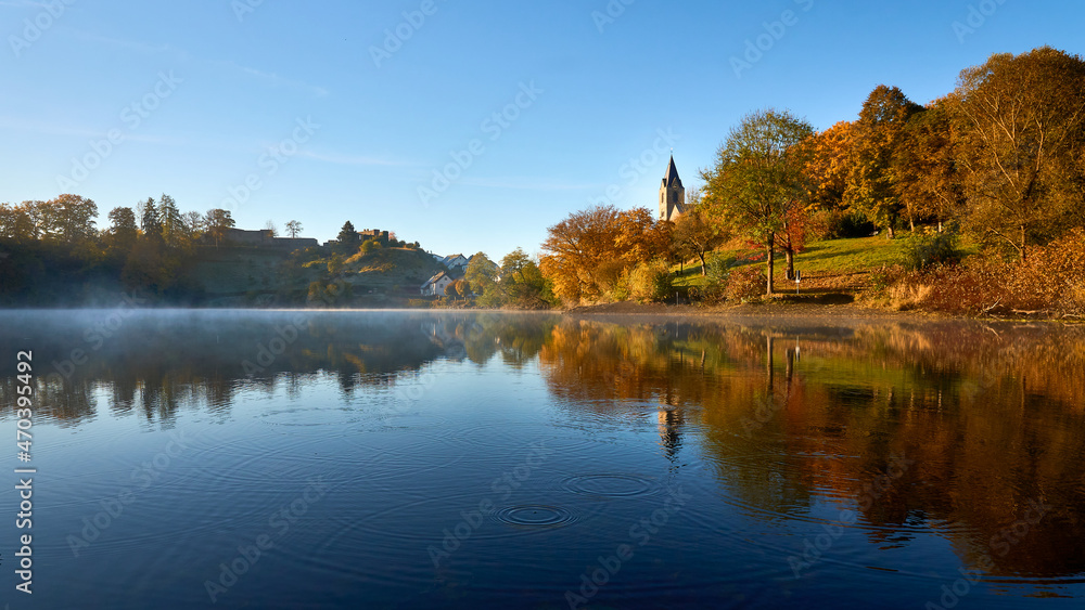 Herbststimmung am Ulmener Maar mit Mathias-Kirche und Burgruine am Morgen mit Nebel über das Wasser und Spiegelung