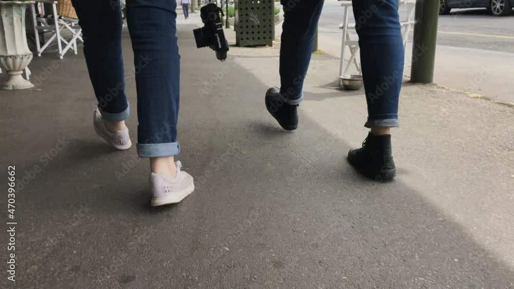 two women walking, view of their feet, one is carrying a film camera two women walking, view of their feet, one is carrying a film camera