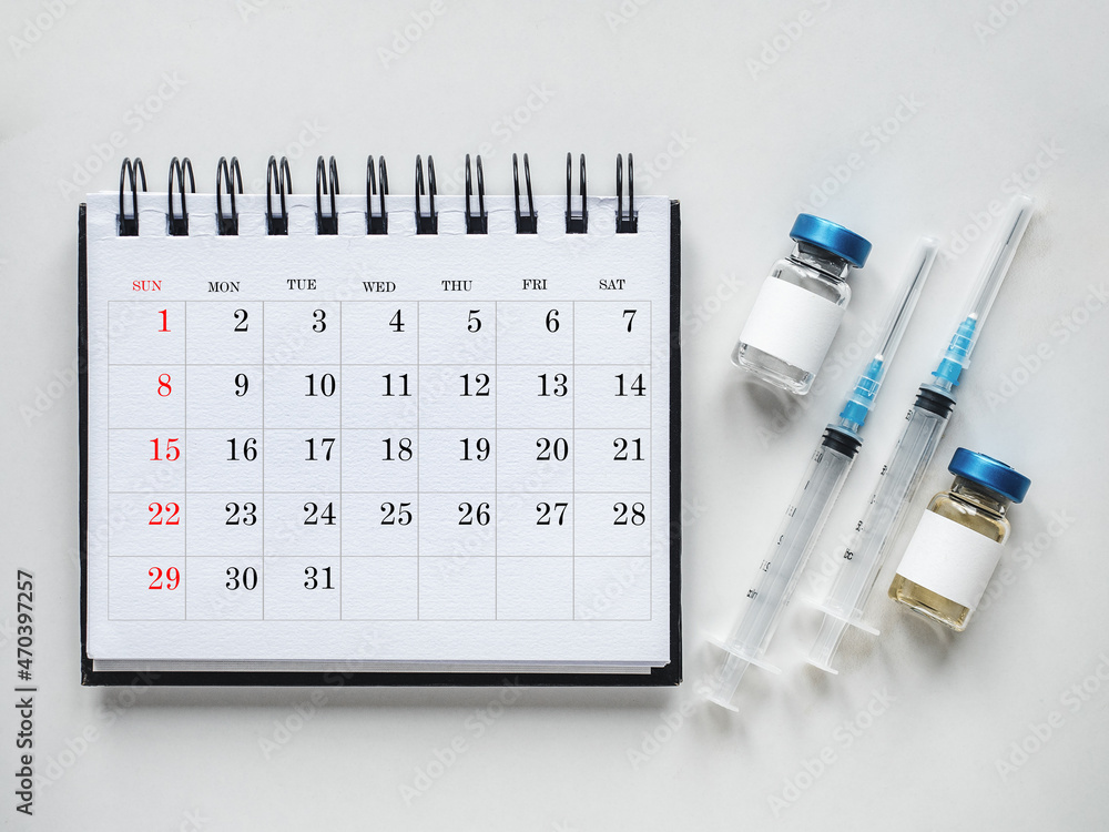 Syringes, injection vials and a calendar page lying on the table. Close-up, indoors, top view. Day light, studio photo. Healthcare concept