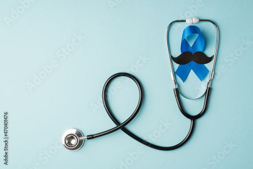 Top view photo of stethoscope and blue ribbon with mustache shape symbol of prostate cancer awareness on isolated pastel blue background with copyspace photo