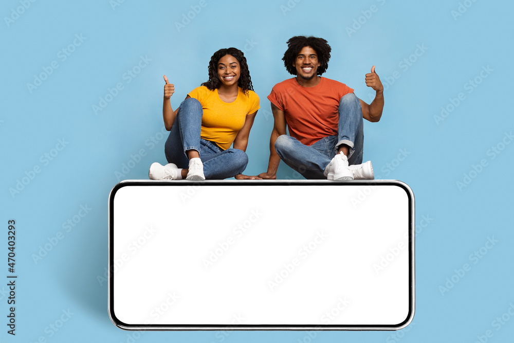 Smiling african american couple sitting on big cellphone
