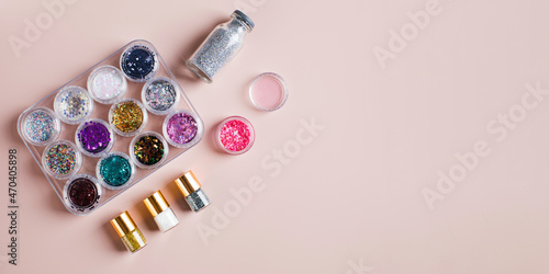 Collection of bottles with colorful sparkles and sequins for nail decor on a light pink background, top view. Copy space