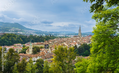 View of the medieval city of Bern, capital of Switzerland, with a foreground of trees and cloudy sky in the background.
