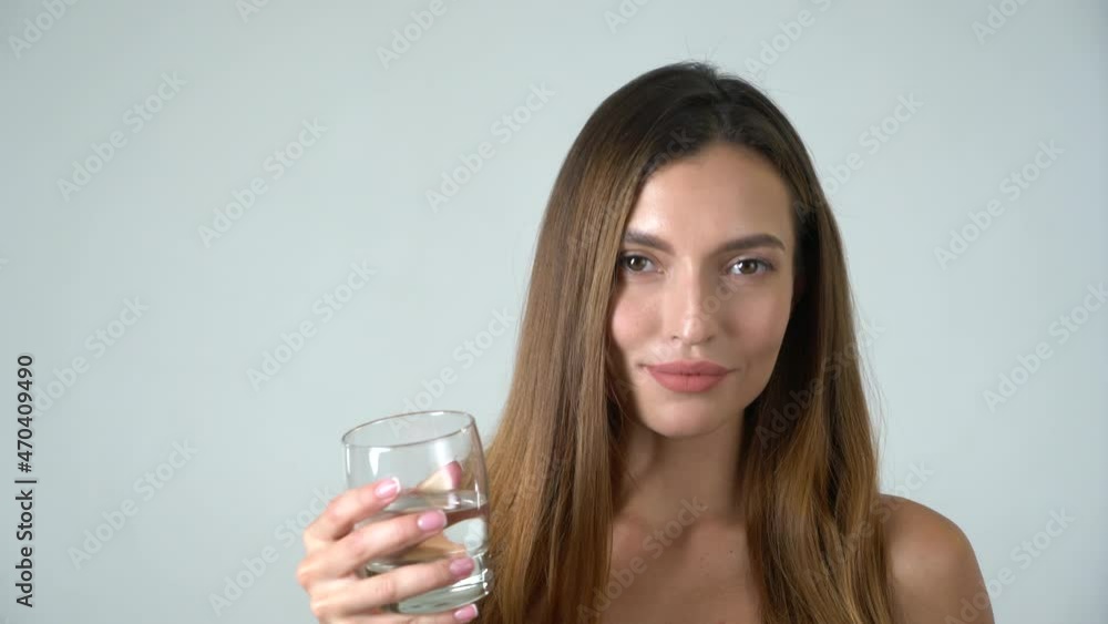 Young attractive caucasian female model drinks water and looks into camera white background Young attractive caucasian female model drinks water and looks into camera white background