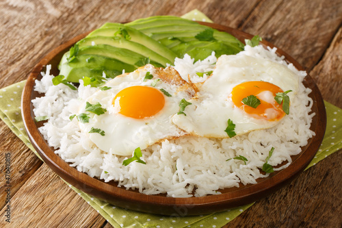 Arroz con huevo is a popular lazy lunch throughout Latin America, consisting of rice that’s topped with a fried egg close up in the plate on the table. Horizontal