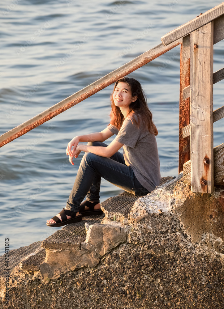 Biracial Asian teen girl relaxing on stone steps leading down to water Biracial Asian teen girl relaxing on stone steps leading down to water