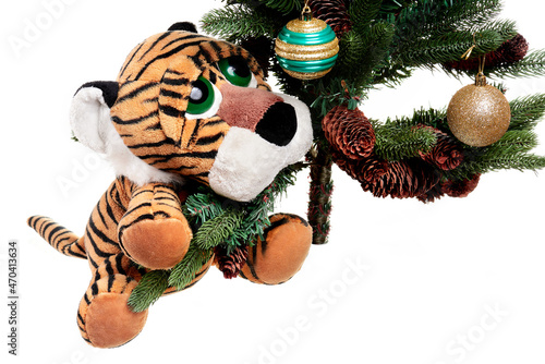 A funny toy tiger cub sits under a Christmas tree and looks at Christmas toys.