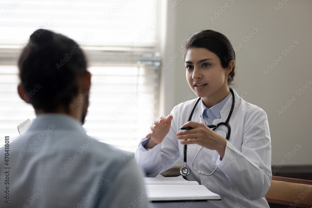 Fototapeta premium Indian woman doctor consulting African American patient at meeting in hospital office, young female physician practitioner talking, explaining, giving recommendation, discussing checkup or symptoms