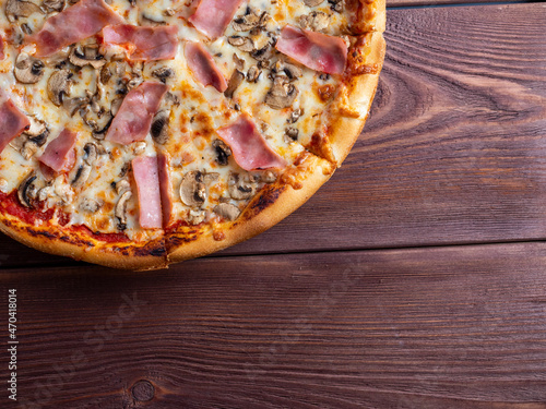 Close-up pizza with ham and mushrooms on a brown wooden background. A traditional Italian dish. A delicious and unhealthy dish. Top view, flat lay, copy space