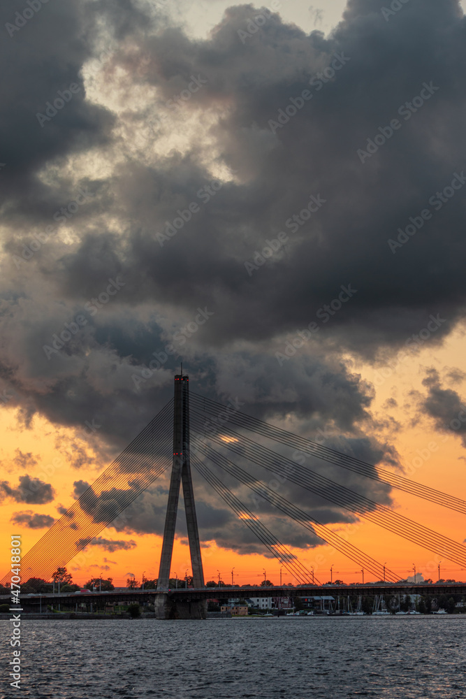 Magnificent sunset over the Daugava river and the Vansu or Suspension bridge in Riga, Latvia. Colorful clouds and warm skylight