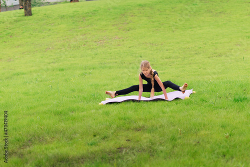 slim girl in a black gymnastic uniform performs gymnastic exercises or pilates on the green grass in the park. Professional gymnast during training 