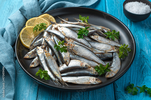 A dish with salted sprat with lemon and parsley on a blue background.