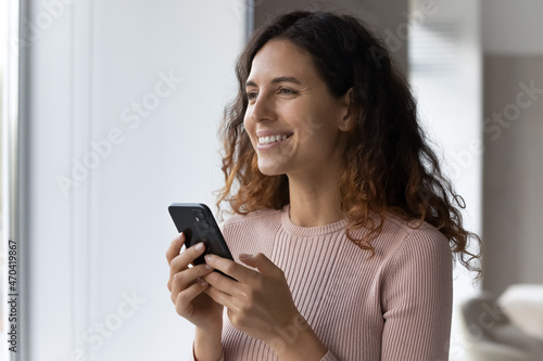 Head shot smiling dreamy woman distracted from modern smartphone, looking in distance, chatting online with boyfriend, waiting for message or phone call, enjoying leisure time with mobile device