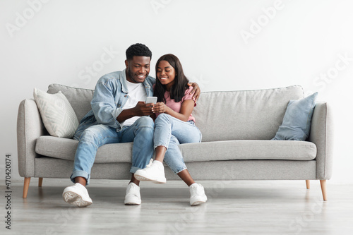 African american couple sitting on couch, using cellphone