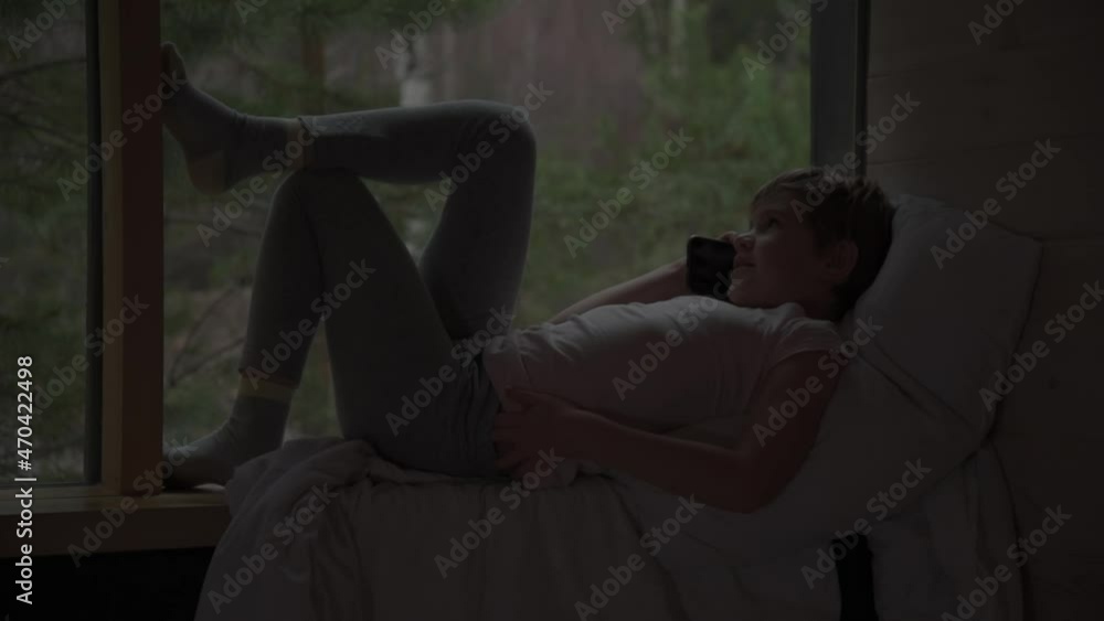 The child is talking on a smartphone at night. The girl clung to the windowsill, lying on the pillow. Secret conversation concept. Secret communication, love The child is talking on a smartphone at night. The girl clung to the windowsill, lying on the pillow. Secret conversation concept. Secret communication, love