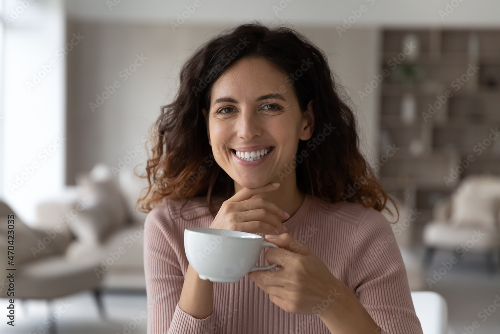 Head shot portrait smiling beautiful hispanic woman holding white cup of tea or coffee, leisure time with hot beverage at home, happy young female looking at camera, enjoying morning, breakfast Head shot portrait smiling beautiful hispanic woman holding white cup of tea or coffee, leisure time with hot beverage at home, happy young female looking at camera, enjoying morning, breakfast