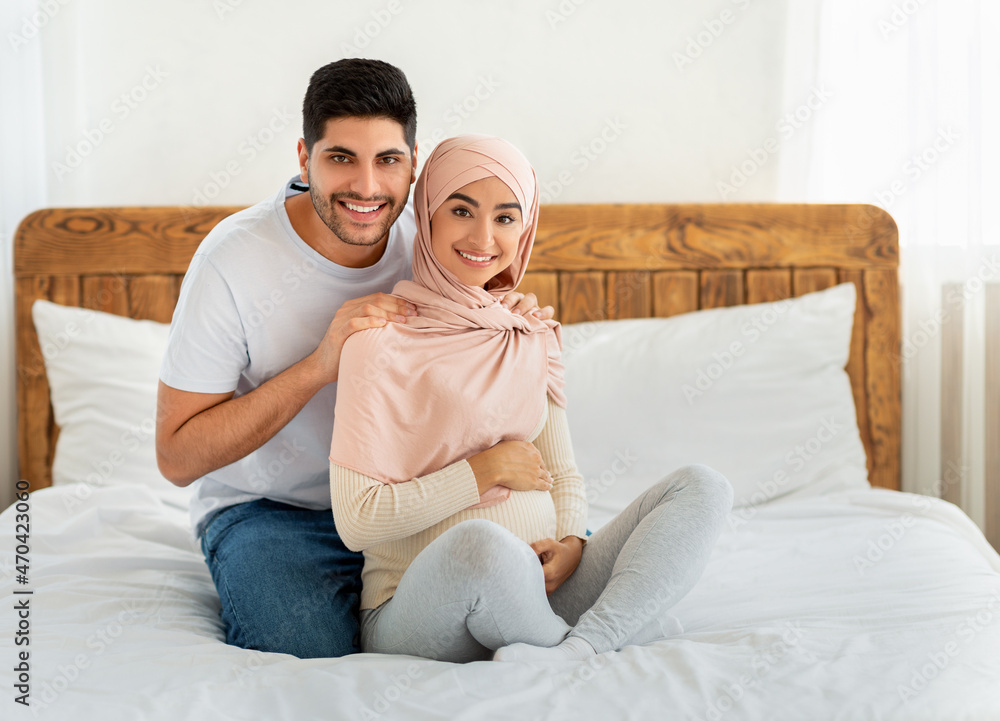 Caring arab husband massaging his pregnant wife's shoulders at home, sitting together on bed Caring arab husband massaging his pregnant wife's shoulders at home, sitting together on bed