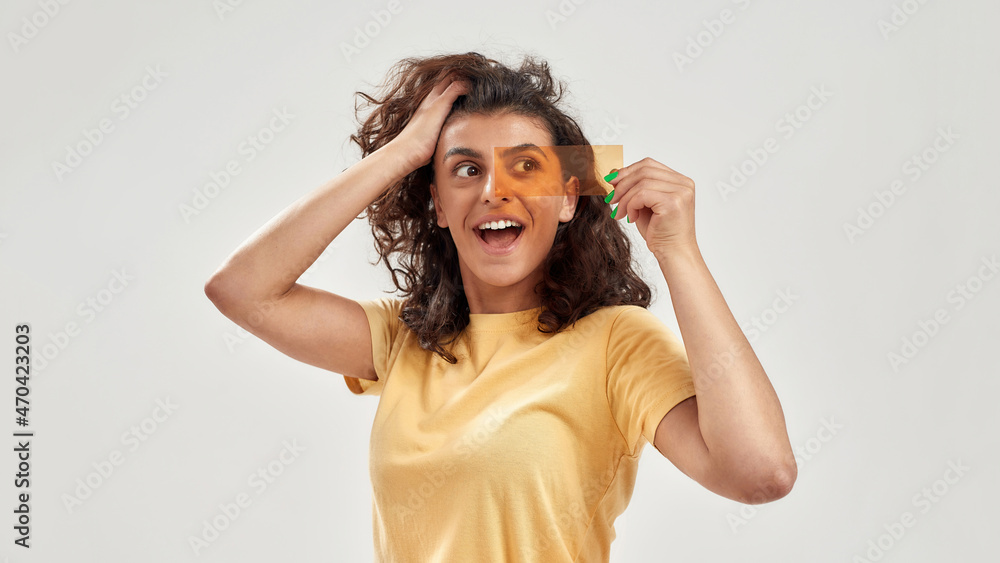 Excited woman holding orange film in front of her eyes, looking aside, posing isolated over light background Excited woman holding orange film in front of her eyes, looking aside, posing isolated over light background