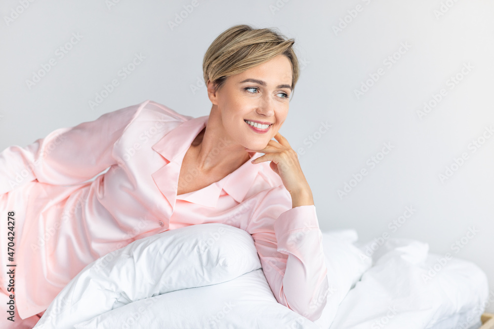 Happy middle-aged woman looking away and thinking in bed Happy middle-aged woman looking away and thinking in bed