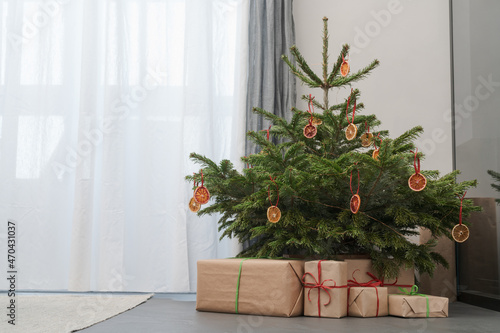 Small christmas tree with gifts in paper wrap near window
