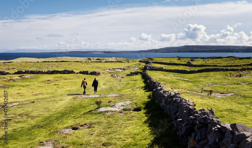 Beautiful landscape scenery of green field and stone wall with people passing by at Aran islands in County Galway, Ireland  photo
