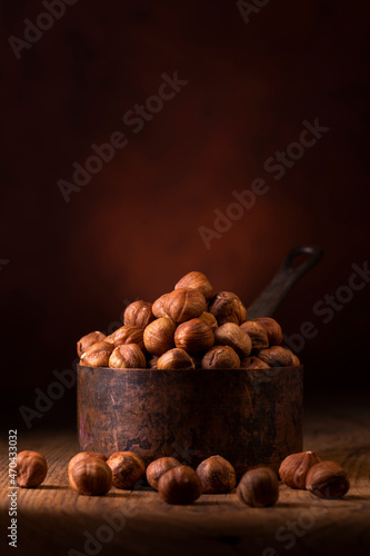 In the foreground, a group of shelled hazelnuts in an aged metal measuring cup against a dark background photo