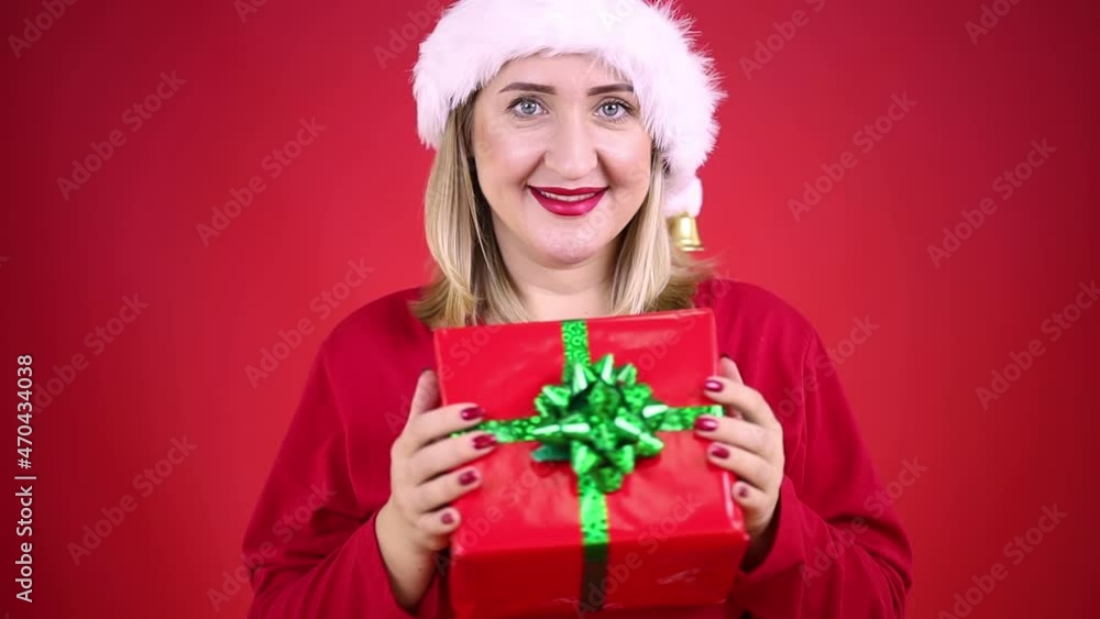 woman, blonde in a Santa Claus hat, holds a gift in front of her and sways woman, blonde in a Santa Claus hat, holds a gift in front of her and sways