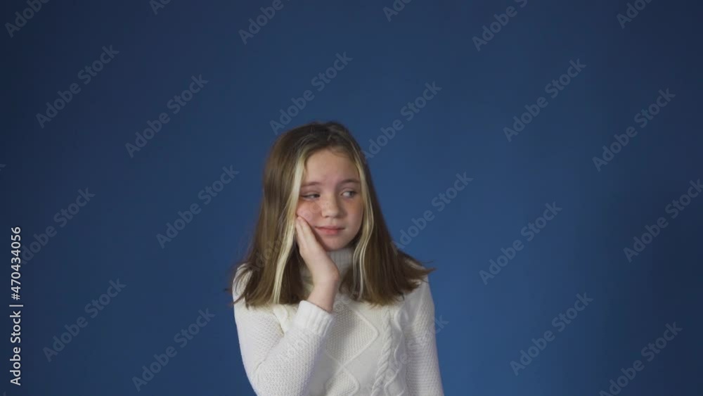 A little girl hurts her tooth against a blue background. Rubs her cheek and is sad A little girl hurts her tooth against a blue background. Rubs her cheek and is sad