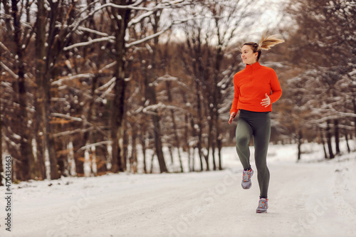 Sportswoman jogging in nature on a snowy winter day. Cold weather, snow, healthy life, fitness, healthy habits, woods