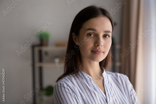 Close up head shot portrait of smiling beautiful young 30s dreamy woman posing at home. Happy pleasant millennial generation lady with perfect skin looking at camera, feeling confident indoors.