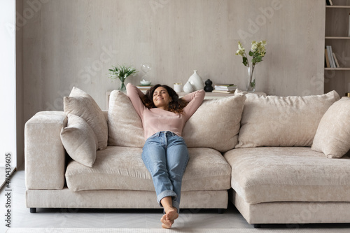 Smiling barefoot woman resting on comfortable couch at home alone, happy beautiful young female with closed eyes stretching, daydreaming or taking day nap, enjoying leisure time, no stress concept photo