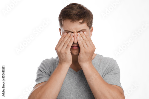 Fototapeta Naklejka Na Ścianę i Meble -  Upset tired sad young caucasian man rubs eyes, suffers from dryness, isolated on white background