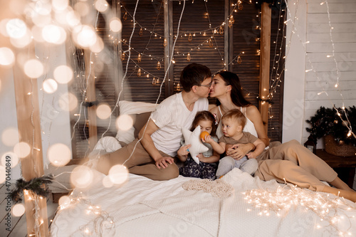Young family playing with children on bed in bedroom decorated for christmas © Maria