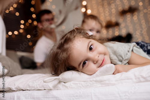 Little girl lies on the bed at home against the background of Christmas lights