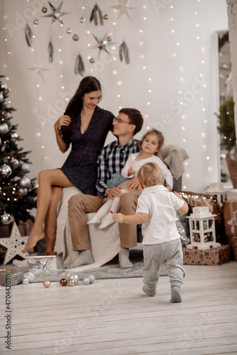 Young parents and children decorate christmas tree in living room at home
