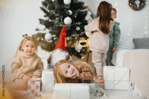 A group of children under a Christmas tree at home. Boys and girls in fancy costumes celebrate winter holidays. Children open gifts by the fireplace.