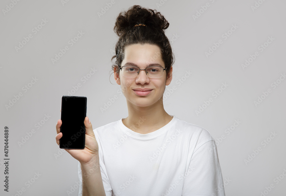 young curly male teenager holding a smartphone in his hands. Gray background young curly male teenager holding a smartphone in his hands. Gray background