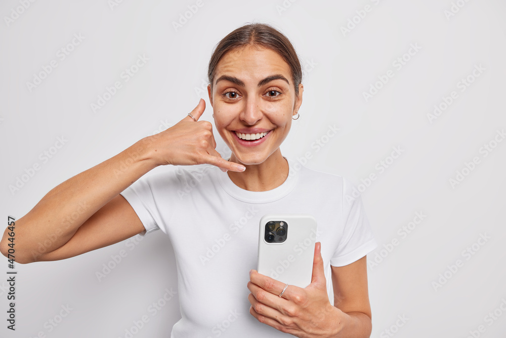 Positive female model asks for telephone number makes call me gesture holds mobile phone has friendly face expression smiles gladfully isolated over white background stays in touch with friend Positive female model asks for telephone number makes call me gesture holds mobile phone has friendly face expression smiles gladfully isolated over white background stays in touch with friend