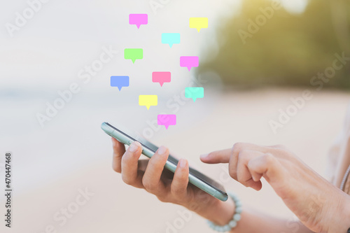 Woman hand using smart phone with message chat icon flying on tropical beach abstract background. Technology business and travel vacation concept.