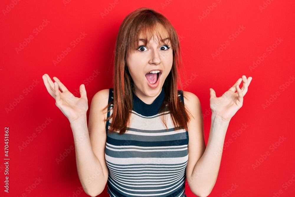 Redhead young woman wearing casual t shirt celebrating crazy and amazed for success with arms raised and open eyes screaming excited. winner concept Redhead young woman wearing casual t shirt celebrating crazy and amazed for success with arms raised and open eyes screaming excited. winner concept
