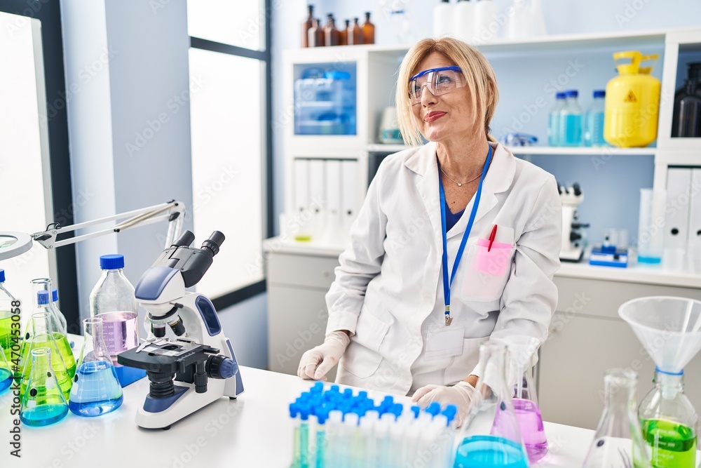 Middle age blonde woman working at scientist laboratory smiling looking to the side and staring away thinking. Middle age blonde woman working at scientist laboratory smiling looking to the side and staring away thinking.