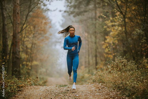 Fotografía Young woman running toward camera on the forest trail at autumn